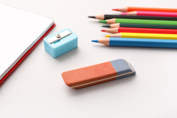 Eraser with sharpener, notebook and colorful pencils on white background