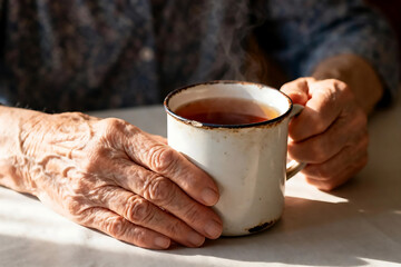 Obraz premium Elderly Mother's Hands Holding Hot Mug of Tea, Warm Intimate Moment Showing Wrinkled Skin Texture, Cinematic Portraiture with Film Grain