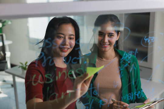 Asian women collaborating on business strategy using glass board