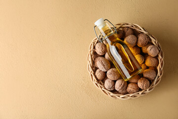 Wicker basket with tasty walnuts and bottle of oil on beige background