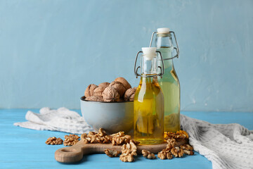 Bowl with tasty walnuts and bottles of oil on wooden table against blue wall