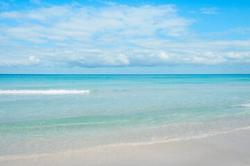 Calm ocean waves gently lap on the sandy shore under a bright blue sky