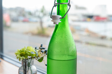 窓辺に置かれた緑色のボトルと小さな花のアレンジメント
