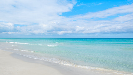 Fototapeta premium Calm ocean waves gently lap on the sandy shore under a bright blue sky