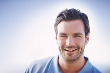 Fototapeta premium Blue sky, portrait and smile of man outdoor in natural environment for break or summer wellness. Confident, happy and mockup space with male person in nature to relax for morning or weekend.