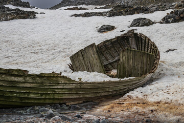 Remains of an ancient boat, on the rocky shore of one of the Antarctic islands. Peninsula. Snow, rocky hills in background.