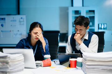 Asian business colleagues feeling stress and fatigue from workload, working late under deadline pressure and tension in modern office.