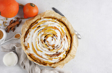 Top view of giant cinnamon pumpkin roll with buttercream frosting,, white marble table. High quality photo, copy space