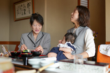 Obraz premium A woman is holding a baby while another woman sits behind her. The two women are smiling and seem to be enjoying each other's company