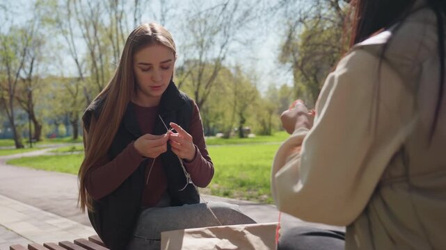 focus on craftsmanship amid tranquil park surroundings and gentle activity, two friends engaged in meticulous bead threading within peaceful park setting demonstrating artistic dedication