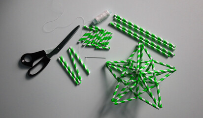 Stars made of straws for cocktails. In green and white stripe. Needle and white thread, scissors, cocktail tubes of different lengths. On white background. Handmade. Ideas for decoration. Christmas.