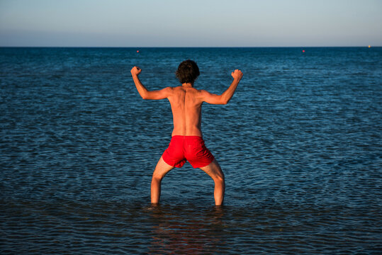 Slim guy posing in red swimwear in sea water