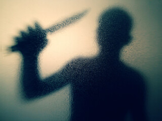 Eerie silhouette of a figure wielding a knife behind frosted glass creates suspense and mystery for true crime stories and psychological thrillers