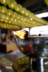 Burning oil lamp in a temple with yellow lanterns in the background