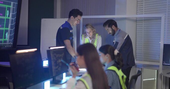 Engineers in high visibility vests collaborate in control room, reviewing digital site plans and dashboards during an operations and safety discussion. Coordination, monitoring, and incident readiness