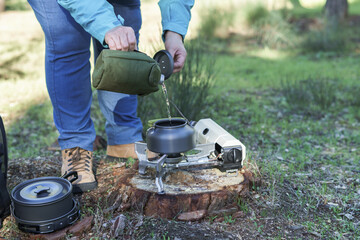 Woman hiker pouring water into a kettle to make it drinkable on a camping stove.