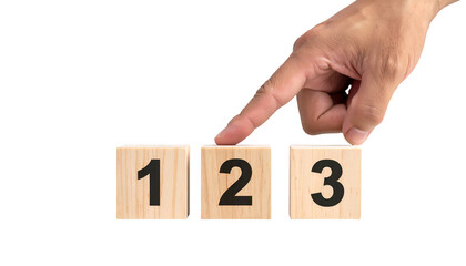 A hand selects the number two on wooden blocks numbered one through three against black