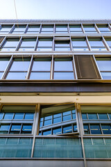 Modern glass facade reflects neighboring buildings in urban setting during daylight hours