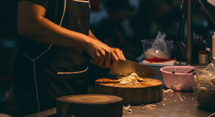 Skilled hands of a chef chopping fresh ingredients on a rustic wooden cutting board with a large knife, food preparation.