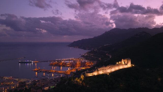 Glowing Medieval Fortress Perched On A Hilltop Overlooking The City And The Gulf of Salerno, Italy. Aerial Drone Shot