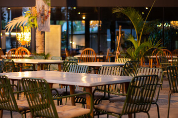 Outdoor dining area with modern tables and chairs under warm evening lights, creating a cozy and inviting café atmosphere.