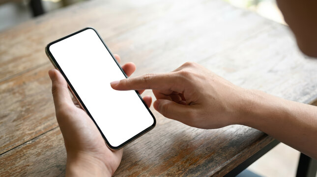 A person's hands holding and interacting with a modern smartphone on a wooden table with the screen transparent and ready for content mobile touching technology