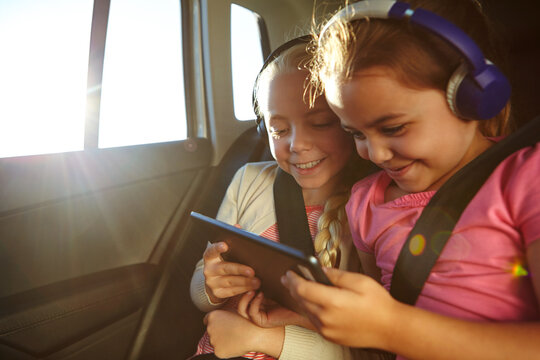 Road trip, headphones or kids with tablet in backseat of car, summer vacation or streaming movie on journey. Watch cartoon, flare or girls smile with tech for entertainment, travel holiday or vehicle