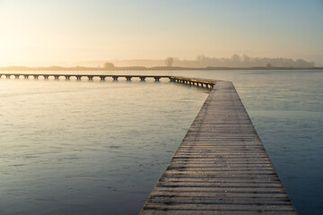 Fototapeta premium Hoarfrost on a jetty (Knuppelpad) in nature reserve Roegwold during a cold, autumn sunrise.