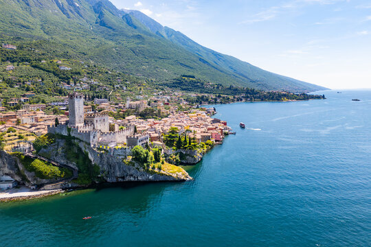 Malcesine Castle on cliff by the lake, aerial view. Stone fortress above Lake Garda with clear view of town and shoreline