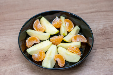 Colorful mix of crisp apple wedges and juicy tangerine slices arranged in a black bowl, creating a fresh and vibrant fruit snack ideal for healthy mornings, meal prep or light refreshing treats.