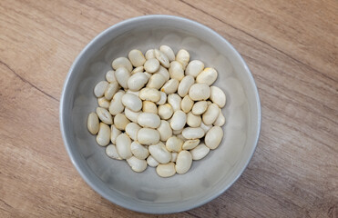 A bowl filled with raw white beans on a wooden surface, suitable as a healthy ingredient for cooking and food preparation.