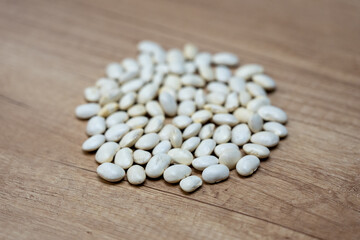 Pile of dried white beans on a wooden surface in a close-up view, suitable for themes of food, ingredients, cooking and legumes.