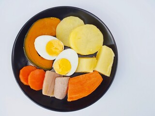 Steamed food is placed on a plate with carrots, potatoes, pumpkin, bananas and boiled chicken eggs. Healthy food.