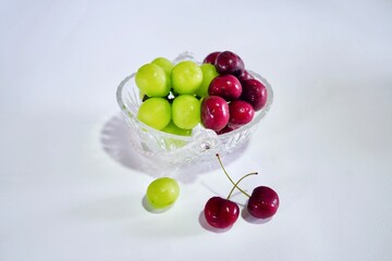 Fruits are placed on a glass basket on a white background. There are , grapes, cherries .