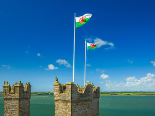 The national flag of Wales waving above the stone turrets against a blue sky and sea (Caernarfon, Wales, United Kingdom)