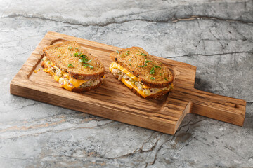 Delicious fresh tuna melt toasts made from rye bread, canned tuna with vegetables and mayonnaise and melted cheese close-up on a wooden board on the table. Horizontal