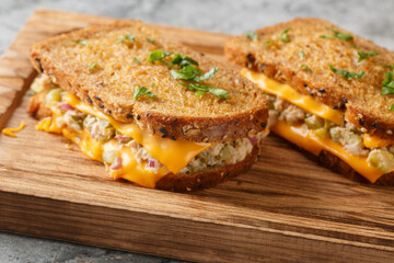 Cheesy tuna melt hot toast with red onion, capers and melting cheese closeup on wooden board on the table. horizontal