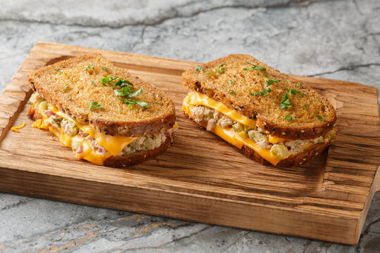 Homemade tuna melt toasts made from buttered bread, canned tuna with vegetables, mayonnaise and melted cheese close-up on a wooden board on the table. Horizontal