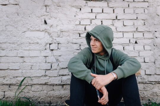 Young man sitting against brick wall contemplating future