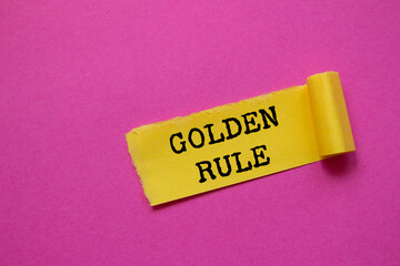 Golden rule message written on ripped torn yellow paper piece on pink background. Conceptual golden...