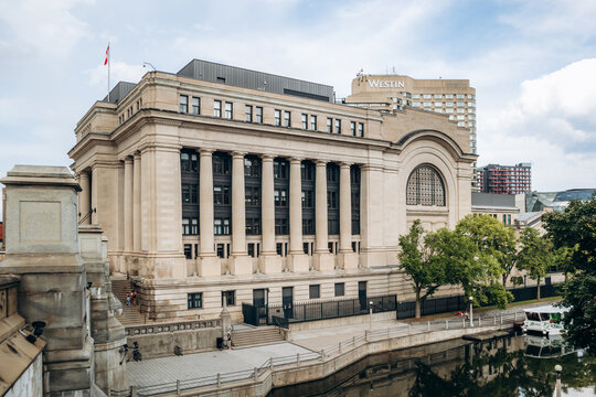 Ottawa, Canada - August 13, 2025: Exterior view of the Senate of Canada Building in downtown Ottawa, with neoclassical columns, a canal in the foreground, and city hotels and towers in the background.