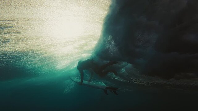 Surfer dives under the ocean wave with surfing board and passes it. Underwater view of the surfer doing duck dive trick