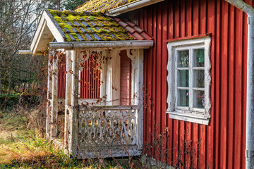 Red idyllic wooden cottage with a veranda and a overgrown garden © Lars Johansson