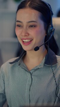 A close-up portrait of a cheerful Asian female customer service representative wearing a headset and smiling happily while talking to a client.