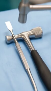 Close-up of surgical instruments including hammers and a chisel on a blue sterile cloth.