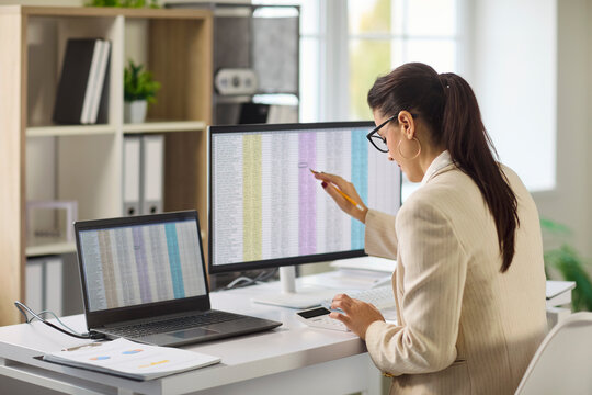 Accountant performs audit analysis on office computer. Woman reviews spreadsheet data, uses calculator, validates accuracy and compliance in office. Clear concept finance control and reporting.