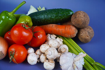 Various vegetables are laid out on the table: celery, carrot, cucumber, tomato, potato, mushrooms, onion, garlic, pepper.