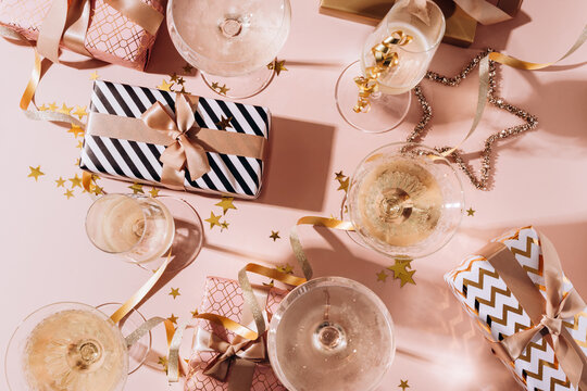 Festive background celebration scene featuring elegant champagne glasses, colorful gift boxes, and shimmering confetti on a soft pink background, perfect for party themes