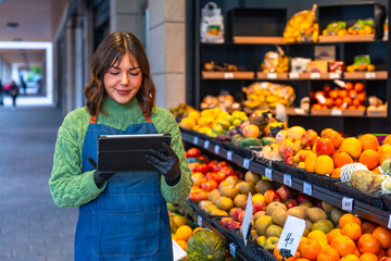 Woman greengrocer using tablet checking fresh produce inventory