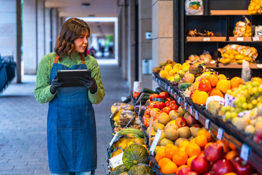 Woman grocer managing inventory using tablet at fruit stand - Powered by Adobe